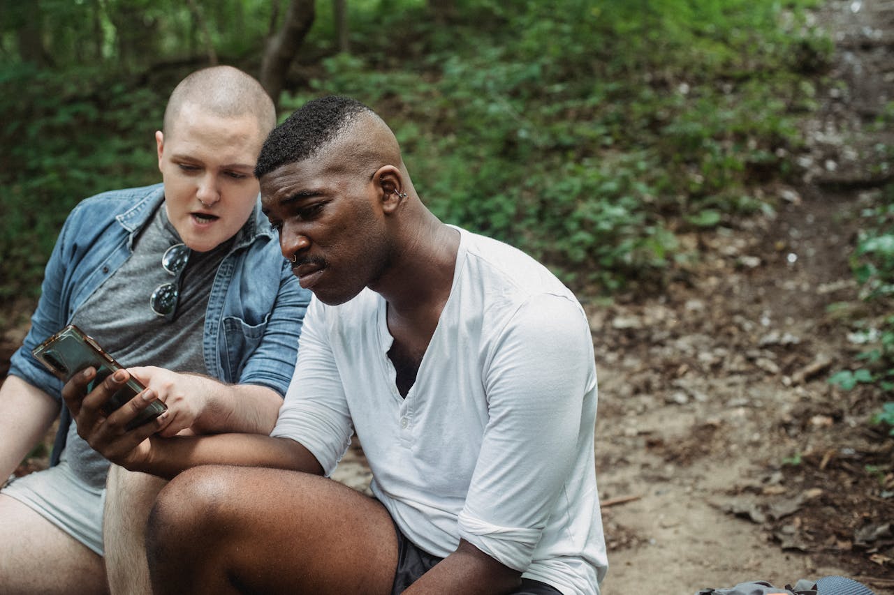 Concentrated diverse hikers searching location with GPS on smartphone while resting in lush green forest in daytime